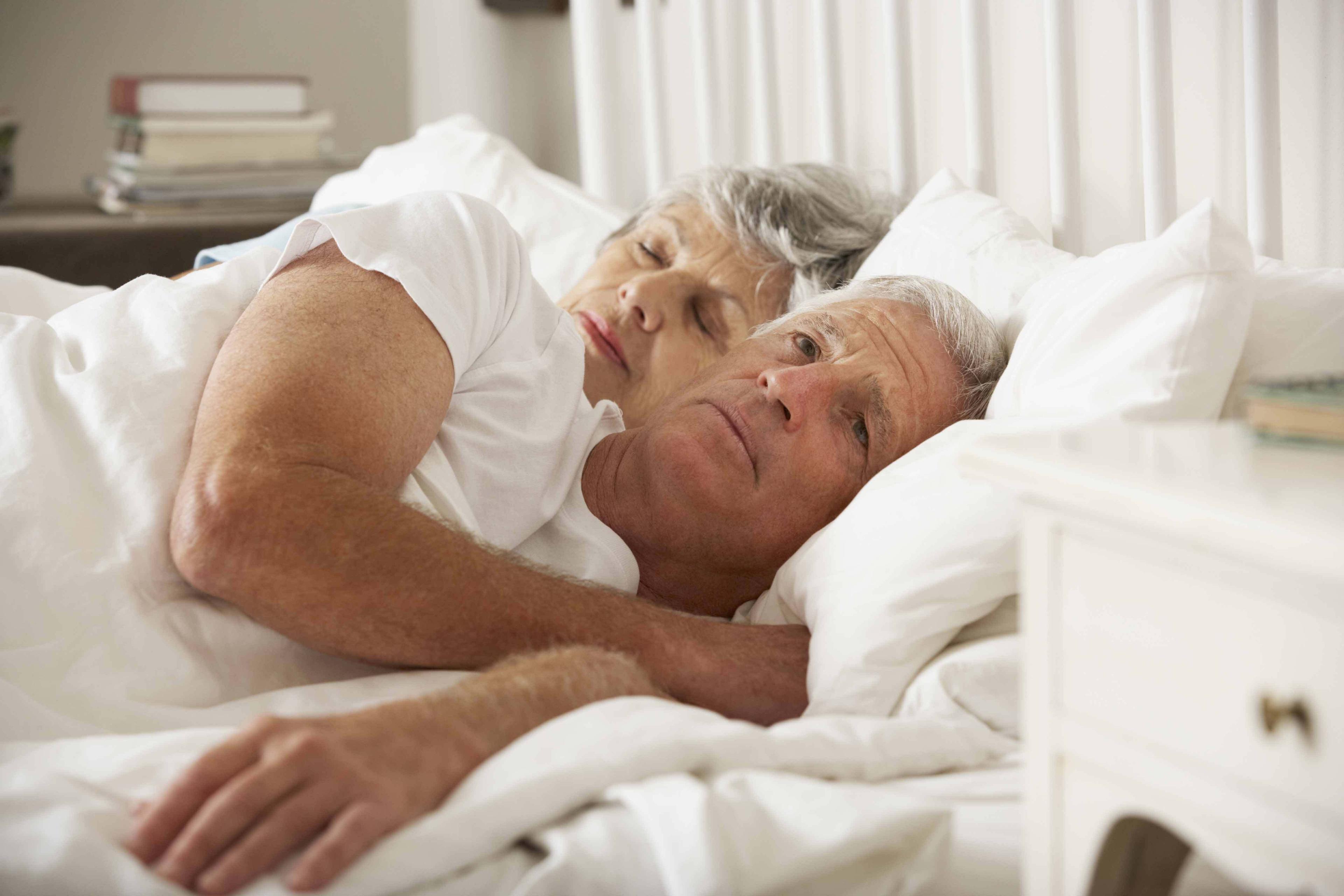 couple âgé dans le lit, la femme dort et l'homme réfléchit